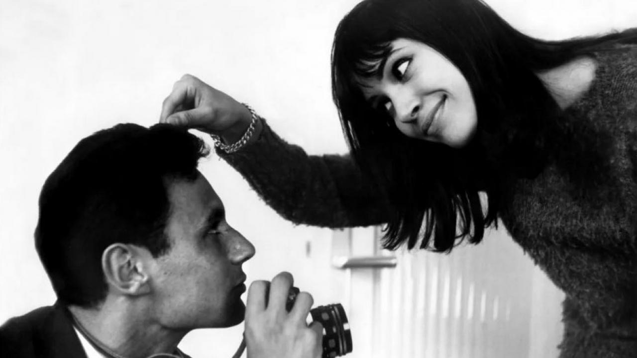 Der kleine Soldat, Szenenbild: Eine Frau beugt sich zu einem Mann mit Fotoapparat herunter und zieht an seinem Haar.