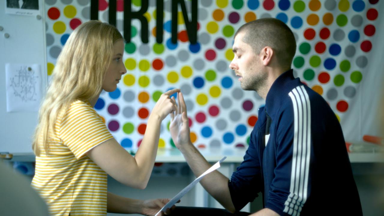 Filmstill aus dem Drama ALS WÄRE ES LEICHT: Eine junge Frau und ein junger Mann mit geschlossenen Augen sitzen sich gegenüber. Die Frau berührt seinen Mittelfinger.