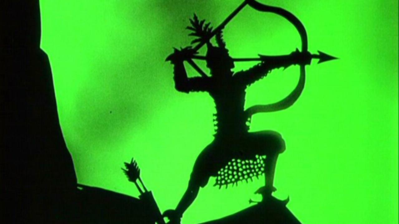 Still aus dem Silhouetten-Trcikfilm DIE ABENTEUER DES PRINZEN ACHMED: Vor grünem Hintergrund ist die schwarze Silhouette eines Bogenschützen zu sehen, der auf einem Felsen steht. Er spannt den Bogen an.