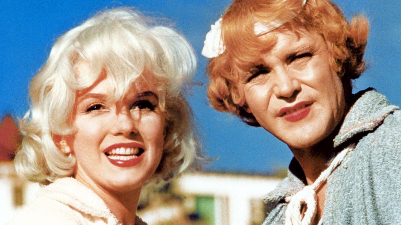 Filmstill aus MANCHE MÖGEN'S HEISS: Großaufnahme einer blonden und einer rothaarigen Frau, die vor blauem Himmel Richtung Kamera schauen. 