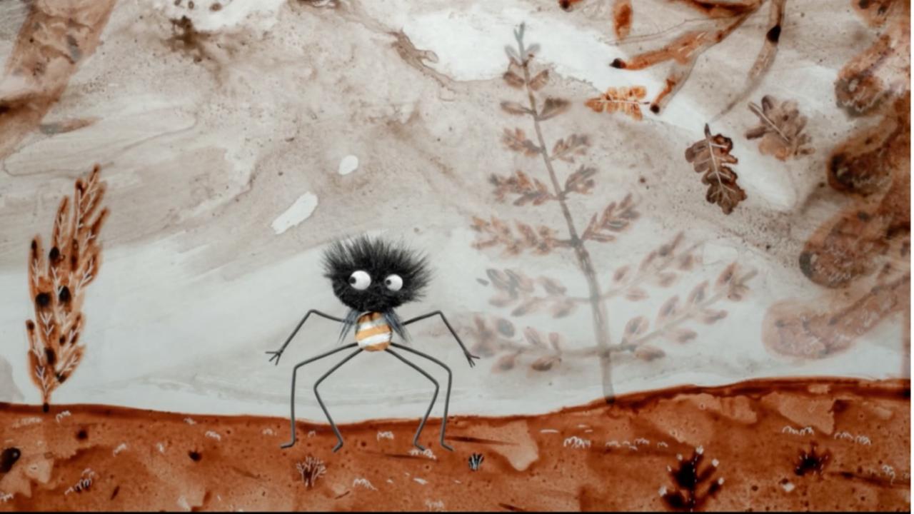 Das Bild zeigt eine stilisierte, fast comicartige Spinnenfigur in einer märchenhaften Landschaft. Die kleine schwarze Spinne besitzt einen kugeligen, zotteligen Körper mit großen weißen Augen und extrem langen, dünnen Beinen. Durch ihren überraschten oder leicht verwirrten Blick wirkt sie eher skurril und liebenswert als bedrohlich.