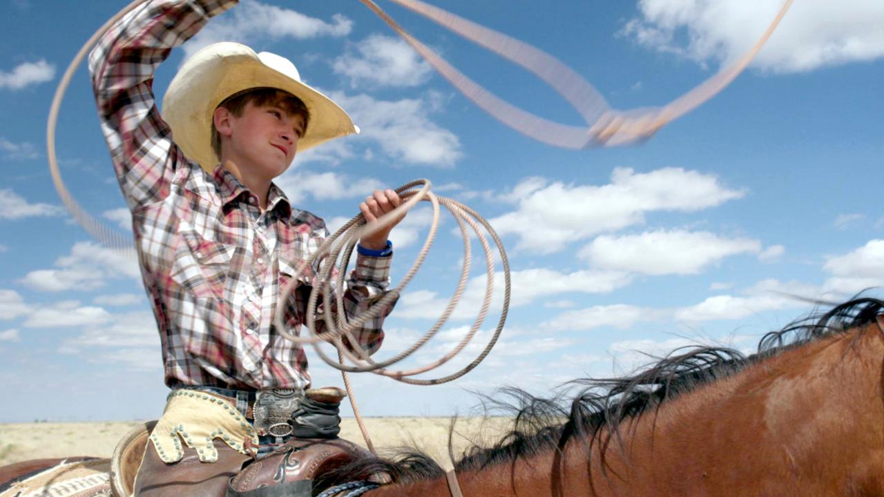 Still aus dem Dokumentarfilm THE COWBOY: Naheinstellung eines Teenagers mit Cowboyhut, der auf einem Pferd sitzt. Er schwingt ein Lasso.