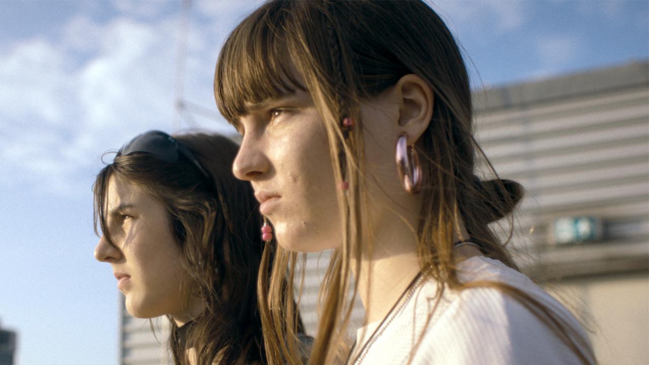 Still aus dem Drama NULPEN: Großaufnahme von zwei 18-jährigen Mädchen; im Hintergrund sind Hochhäuser zu erkennen.