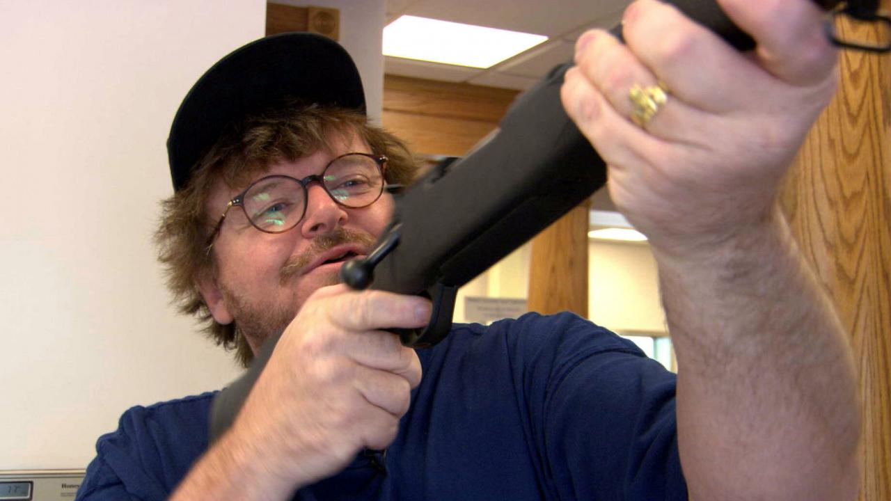 Still aus dem Dokumentarfilm BOLWING FOR COLUMBINE: Der Filmemacher Michael Moore hält ein Gewehr hoch.