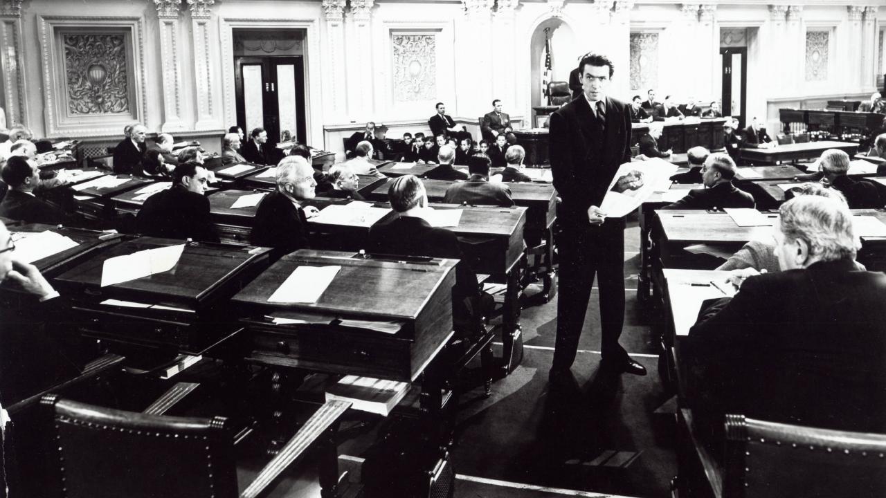 Still aus dem Drama MR. SMITH GEHT NACH WASHINGTON: Die Titelfigur steht im Senat zwischen den dort anwesenden Politikern.