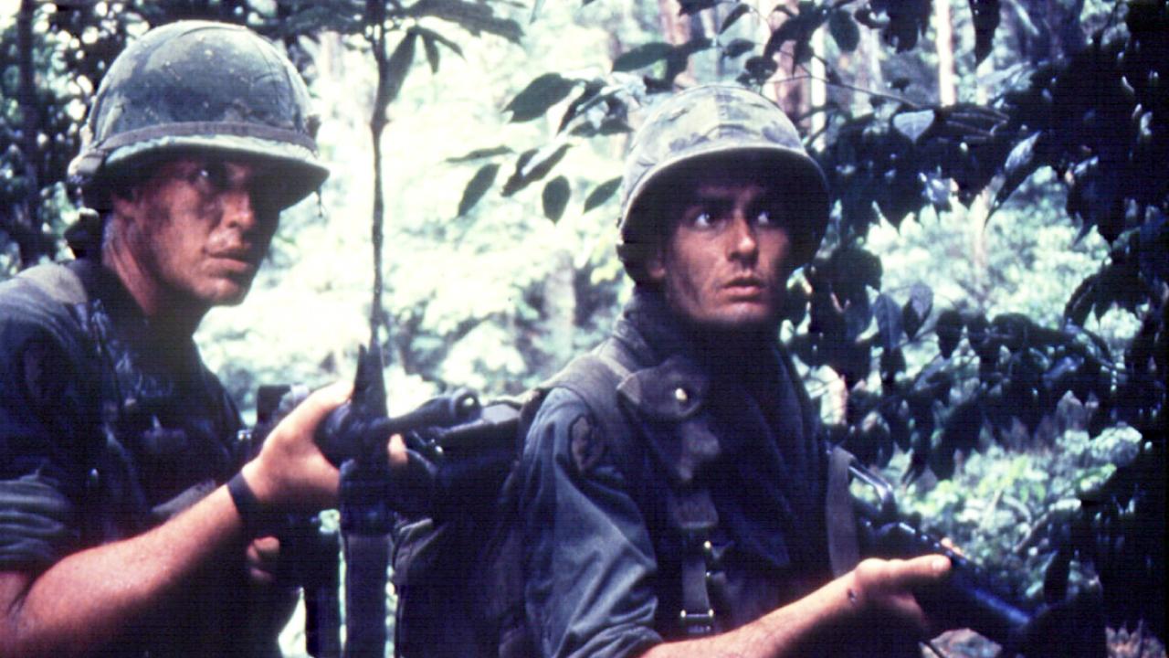 Still aus dem Kriegsdrama PLATOON: Zwei junge US-Soldaten stehen in einem Dschungel mit gezückten Gewehren. Sie wirken angespannt.