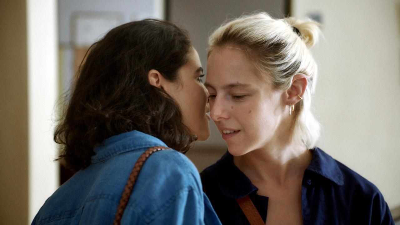 Still aus dem Drama MIT LEISER STIMME: Nahaufnahme von zwei jungen Frauen. Die eine flüstert der anderen etwas ins Ohr.