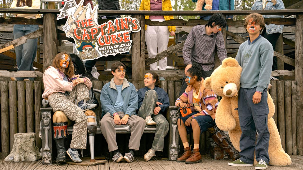 Still aus dem Drama SUNNY DANCER: Eine Gruppe Jugendlicher sitzt und steht vor einem hölzernen Stand auf einem Jahrmarkt. Einige haben bemalte Gesichter. Der Junge rechts hält einen riesigen Teddy im Arm.