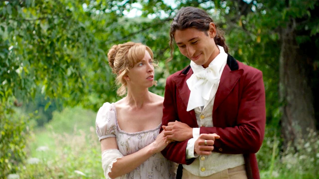 Still aus dem Kurzfilm JANE AUSTEN'S PERIOD DRAMA: Ein junge Frau und ein junger Mann, gekleidet im Stil des 19. Jahrhunderts, laufen eingehakt nebeneinander. Sie scheinen im Gespräch, der Mann lächelt, die Frau schaut ihn ernst an.