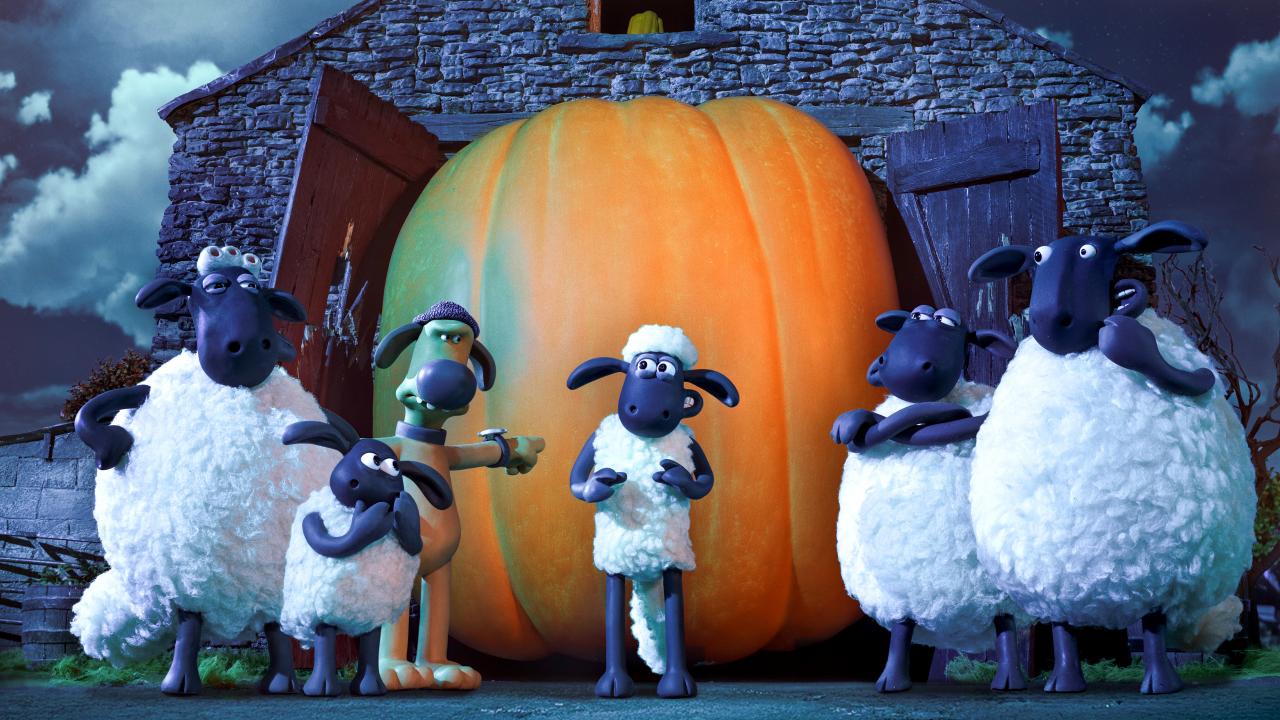 Still aus dem Animationsfilm SHAUN DAS SCHAF – SPUK IM KÜRBISFELD: Shaun das Schaf steht vor einem riesigen Kürbis, der den Eingang vor einem Haus versperrt. Um ihn herum stehen weitere Schafe und ein Hund, der anklagend mit dem Finger auf Shaun zeigt.
