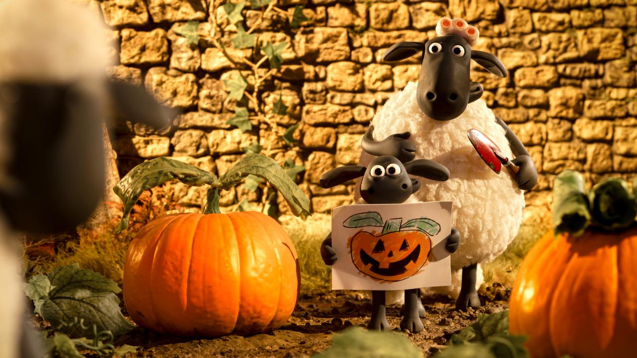 Still aus dem Animationsfilm SHAUN DAS SCHAF – SPUK IM KÜRBISFELD: Ein kleines und ein großes Schaf stehen in einem Kürbisfeld. Das kleine Schaf hält ein gemaltes Bild von einem Halloween-Kürbis in den Händen.
