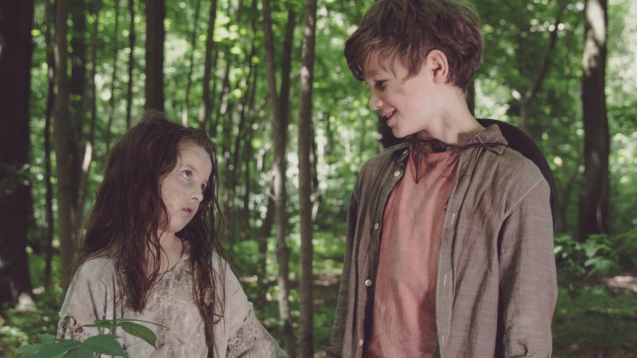 Stil aus dem Kurzfilm ZOMRIELLA: Ein Junge und ein ungewöhnlich blasses und zerzaustes Mädchen stehen im Wald und schauen sich lächelnd an.