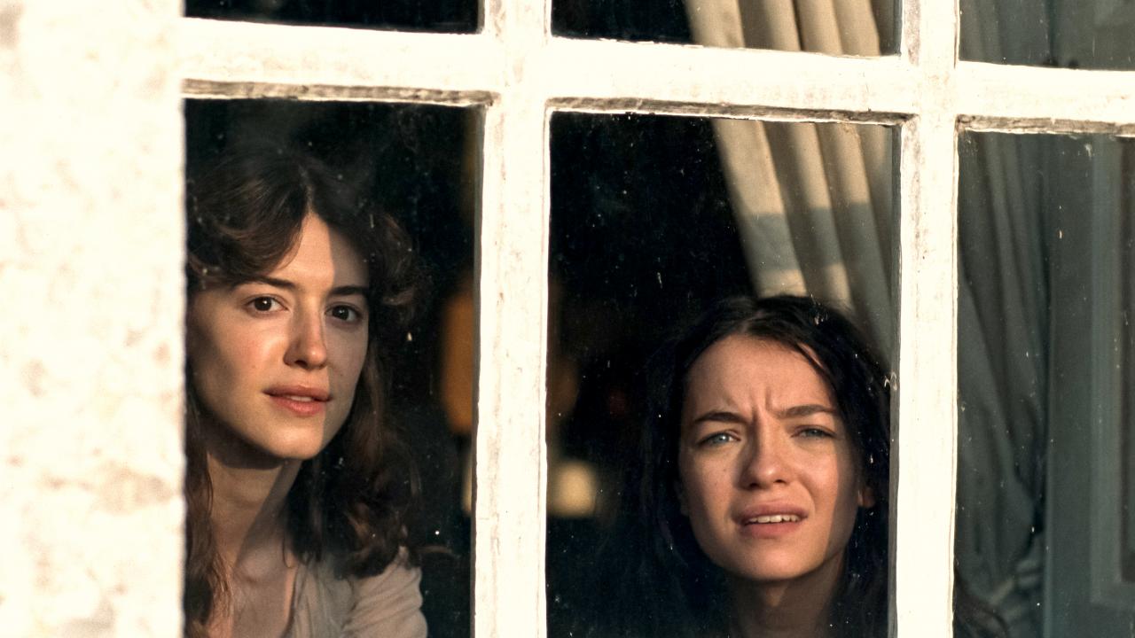 Still aus der Literaturverfilmung SINN UND SINNLICHKEIT: Zwei junge Frauen mit langen Haaren schauen aus einem Fesnter, das in der Außenansicht zu sehen ist.