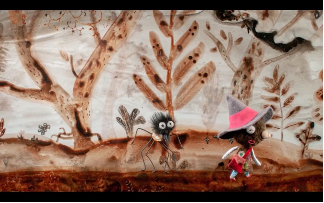 Eine kleine, fantasievoll gekleidete Tierfigur mit großem Hut läuft durch eine märchenhafte Waldlandschaft, dicht gefolgt von einer zotteligen schwarzen Spinne mit langen dünnen Beinen und großen Augen. Die warmen Braun- und Ockertöne sowie die handgemachte Ästhetik verleihen der Szene etwas Poetisches und erinnern an einen animierten Kinderfilm oder ein illustriertes Märchenbuch.